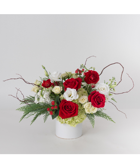 The Good Tidings Christmas Arrangement exudes timeless holiday elegance, beautifully presented in an elegant white ceramic vase.