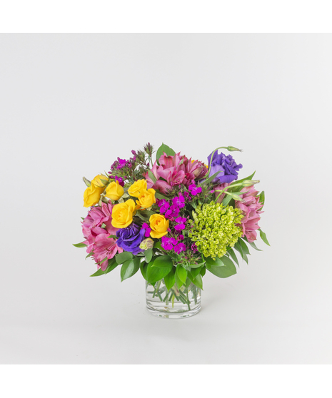 Twilight Fields is a vibrant, garden-inspired floral arrangement that captures the beauty of a colorful meadow at dusk, thoughtfully designed in a classic glass vase.
